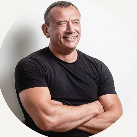 John Kattenhorn, smiling, arms crossed, in a black t-shirt against a light wall